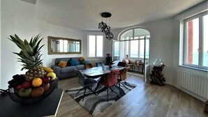 A spacious living area with a dining table, sofa, and a large window providing natural light.