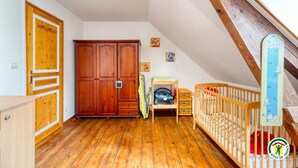 A room with wooden flooring, a wooden wardrobe, a crib, and a ceiling with exposed beams. - Gîtes de France® - Flab'Zen (CRIEL SUR MER)
