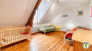 A child's room with a wooden crib, a small bed with a green bedspread, a loft bed with a red blanket, and a desk. - Gîtes de France® - Flab'Zen (CRIEL SUR MER)