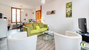 A modern living room with a green sofa, white armchairs, a glass coffee table, and a flat-screen TV. - Gîtes de France® - Flab'Zen (CRIEL SUR MER)
