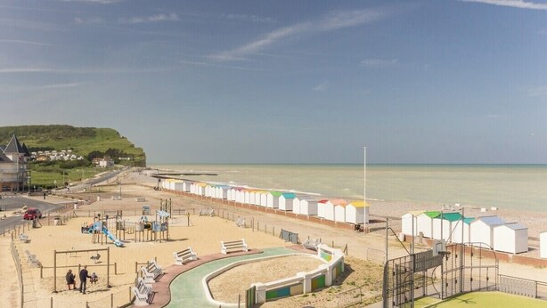 A beachside playground with slides and swings, a sandy area, and beach huts in the background. - Gîtes de France® - Flab'Zen (CRIEL SUR MER)