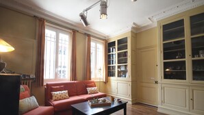 A living room with a red sofa, a coffee table, and a cabinet with glass doors. - Gîtes de France® - Bayen's Family (FECAMP)