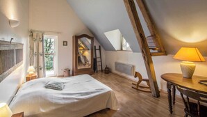 Ein Schlafzimmer mit schrägen Wänden, einem Bett, einer Holzleiter, einem Tisch und einer Lampe.