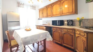 Una cocina con armarios de madera, un refrigerador, un microondas y una mesa de comedor con sillas.