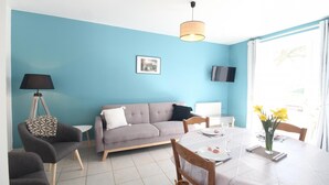 Una sala de estar con un sofá, una mesa de comedor con sillas, una lámpara y un televisor en la pared.