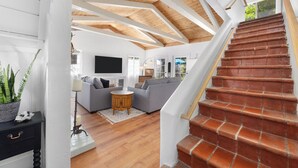A spacious living room with a grey sofa, wooden flooring, and a red brick staircase.