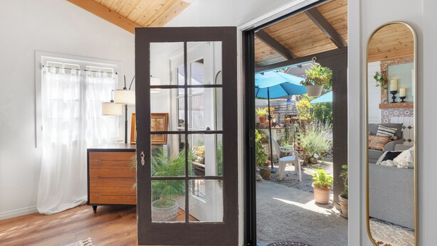 An open door leading to a patio with potted plants and outdoor furniture.