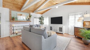 A living room with a grey sofa, wooden ceiling beams, a TV, and a potted plant. - Delightful 1931 Spanish Style abode in the very desirable area, Studio City, CA. (Los Angeles)