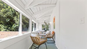 A bright, sunlit corridor with white walls and a green floor, leading to a seating area with wicker chairs and a table.