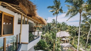 Uma villa moderna com telhado de colmo, uma varanda com vista para vegetação exuberante e uma área de piscina.