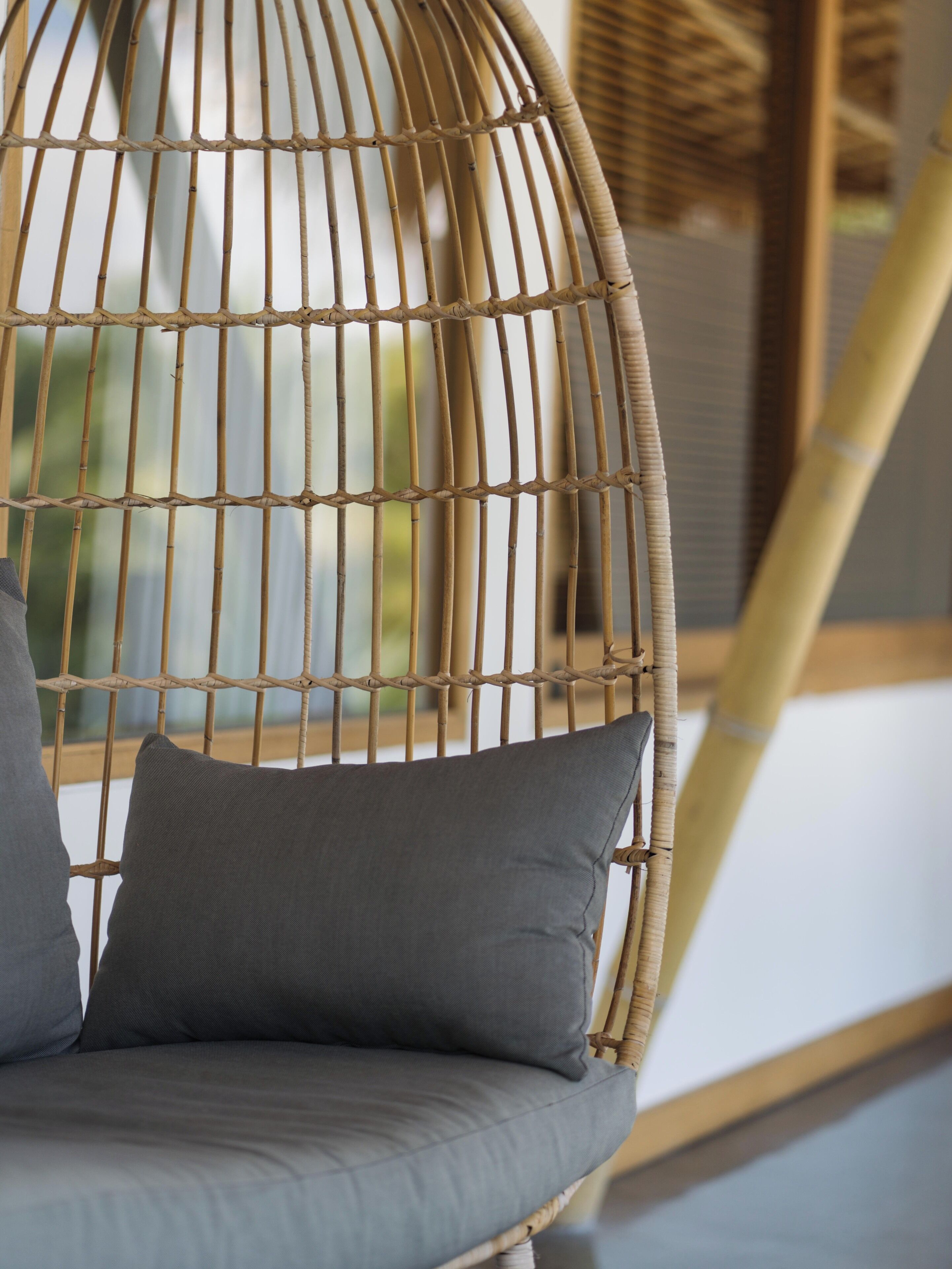 A wicker chair with grey cushions in a room with a bamboo structure.