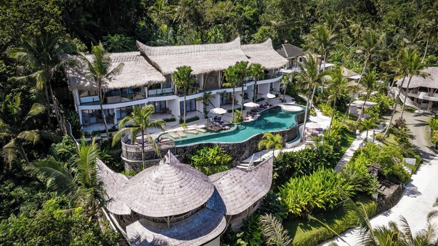 Um resort com uma grande piscina, edifícios com telhados de palha e exuberantes paisagens tropicais.