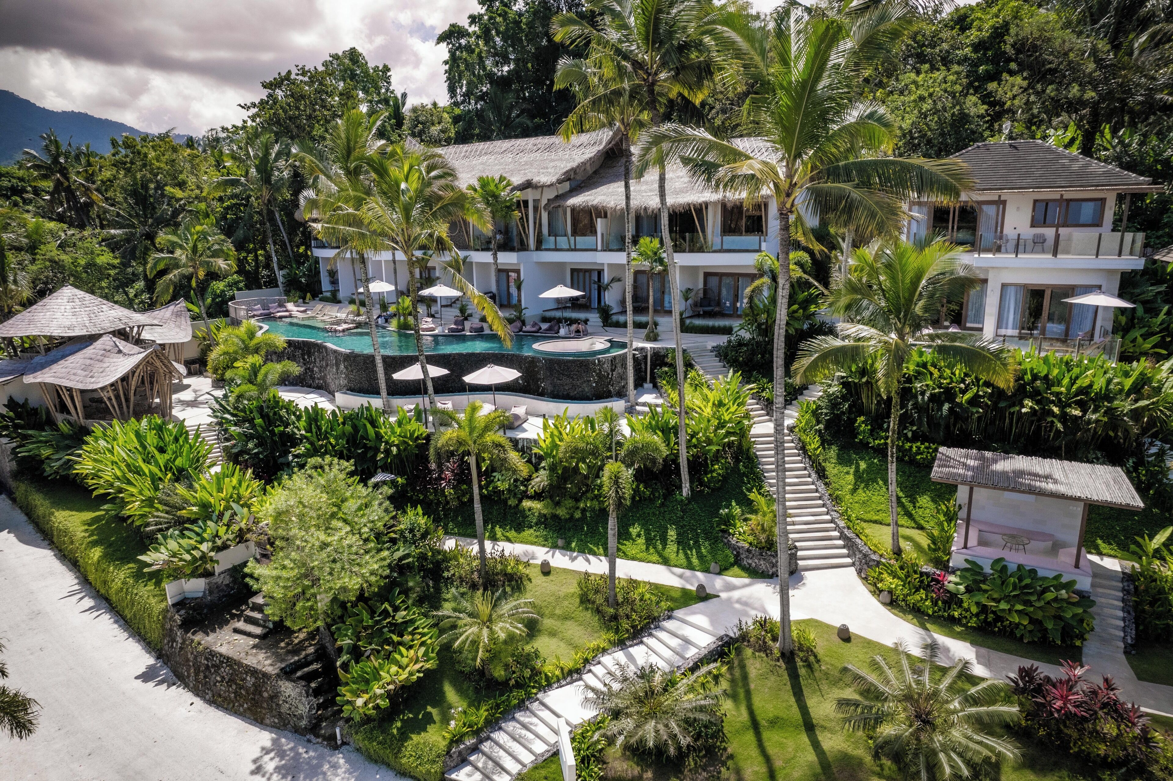 Ein Resort mit Pool, Palmen und einem Gebäude mit einem Reetdach.