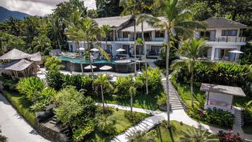 Un resort con piscina, palmeras y un edificio de techo de paja.