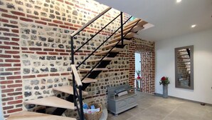 Un interior moderno con pared de ladrillo, escalera de madera, sofá gris y una pequeña mesa con una cesta.