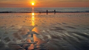 Una playa al atardecer, con el sol reflejado en la arena mojada.
