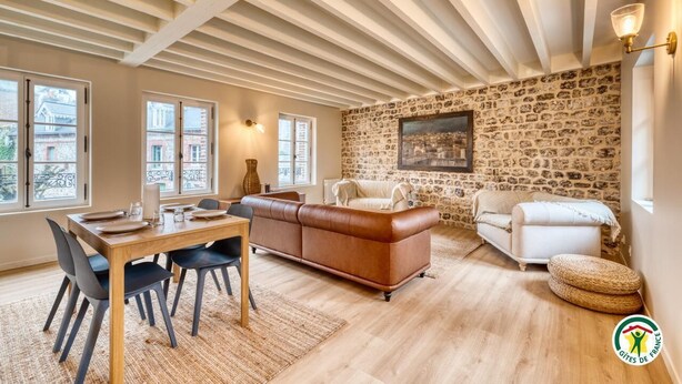 A spacious living area with a dining table, leather sofa, and a stone wall. - Gîtes de France® - Chez Mlle Rose (VEULES LES ROSES)