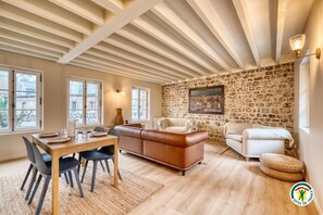 A spacious living area with a dining table, leather sofa, and a stone wall. - Gîtes de France® - Chez Mlle Rose (VEULES LES ROSES)