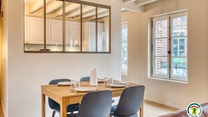 A dining area with a wooden table set for four, a large mirror above the table, and a window with a view of a brick building. - Gîtes de France® - Chez Mlle Rose (VEULES LES ROSES)