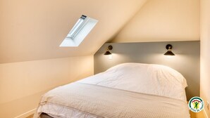 A bedroom with a sloped ceiling, a skylight, and two wall-mounted lamps. - Gîtes de France® - Chez Mlle Rose (VEULES LES ROSES)