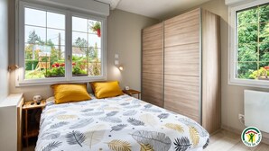 Une chambre à coucher comprenant un lit, deux oreillers, une table de chevet, une fenêtre donnant sur un espace verdoyant et une armoire.