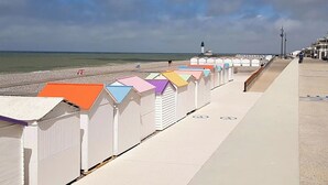 Eine Reihe bunter Strandhäuser entlang einer Uferpromenade, im Hintergrund ein Leuchtturm.