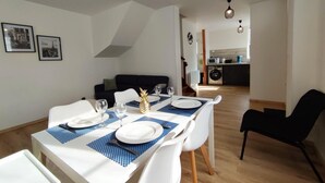 Ein Essbereich mit einem Tisch, gedeckt für vier Personen, weißen Stühlen und einer Ananas als Mittelpunkt. Im Hintergrund ist eine Küche erkennbar.