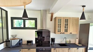 A modern kitchen with wooden cabinets, a built-in oven, a coffee maker, and a sink. - Gîtes de France® - du Mesnil (ECTOT L'AUBER)