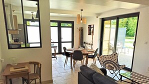 A modern living room with a sofa, dining table, and chairs. There is a large window with a view of the outdoors. - Gîtes de France® - du Mesnil (ECTOT L'AUBER)