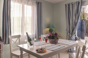 Un comedor con una mesa dispuesta para dos personas, una botella de champán, dos copas, un plato de aperitivos y una planta en maceta.