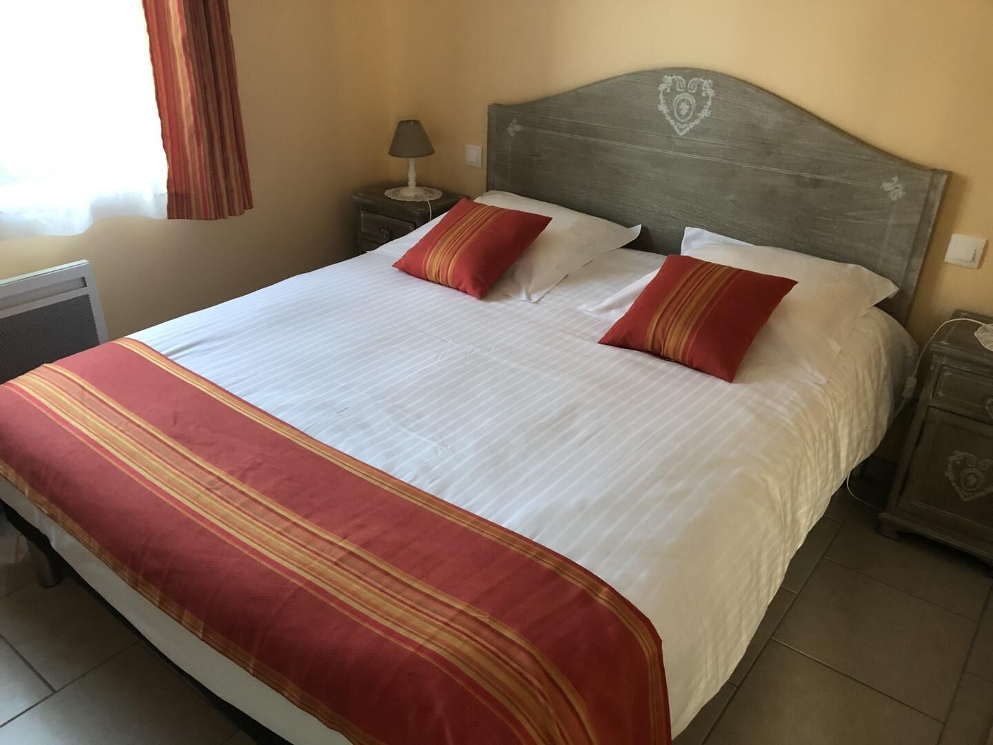 A neatly made bed with a striped red and white bedspread, two matching pillows, and a wooden headboard with a heart design.