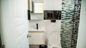 A compact bathroom with a white toilet, a small sink, and a glass-enclosed shower area. - Spacious room (queen size bed) in a hotel in Punta Cana (Punta Cana)