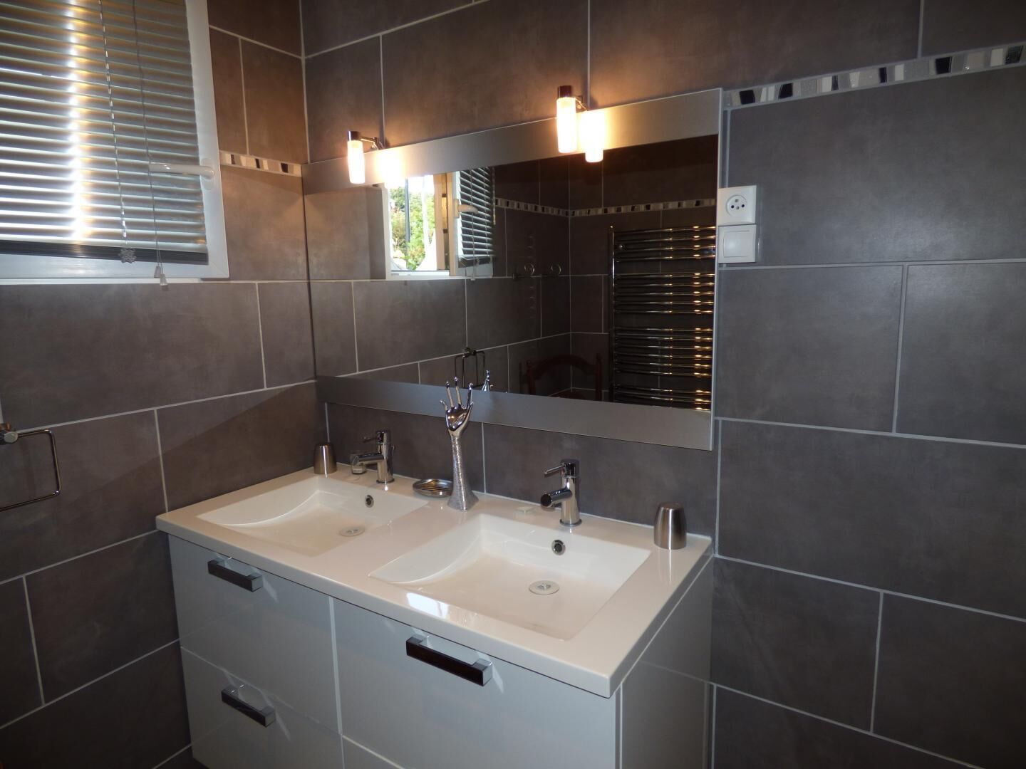 A modern bathroom with two sinks, a large mirror, and overhead lighting.