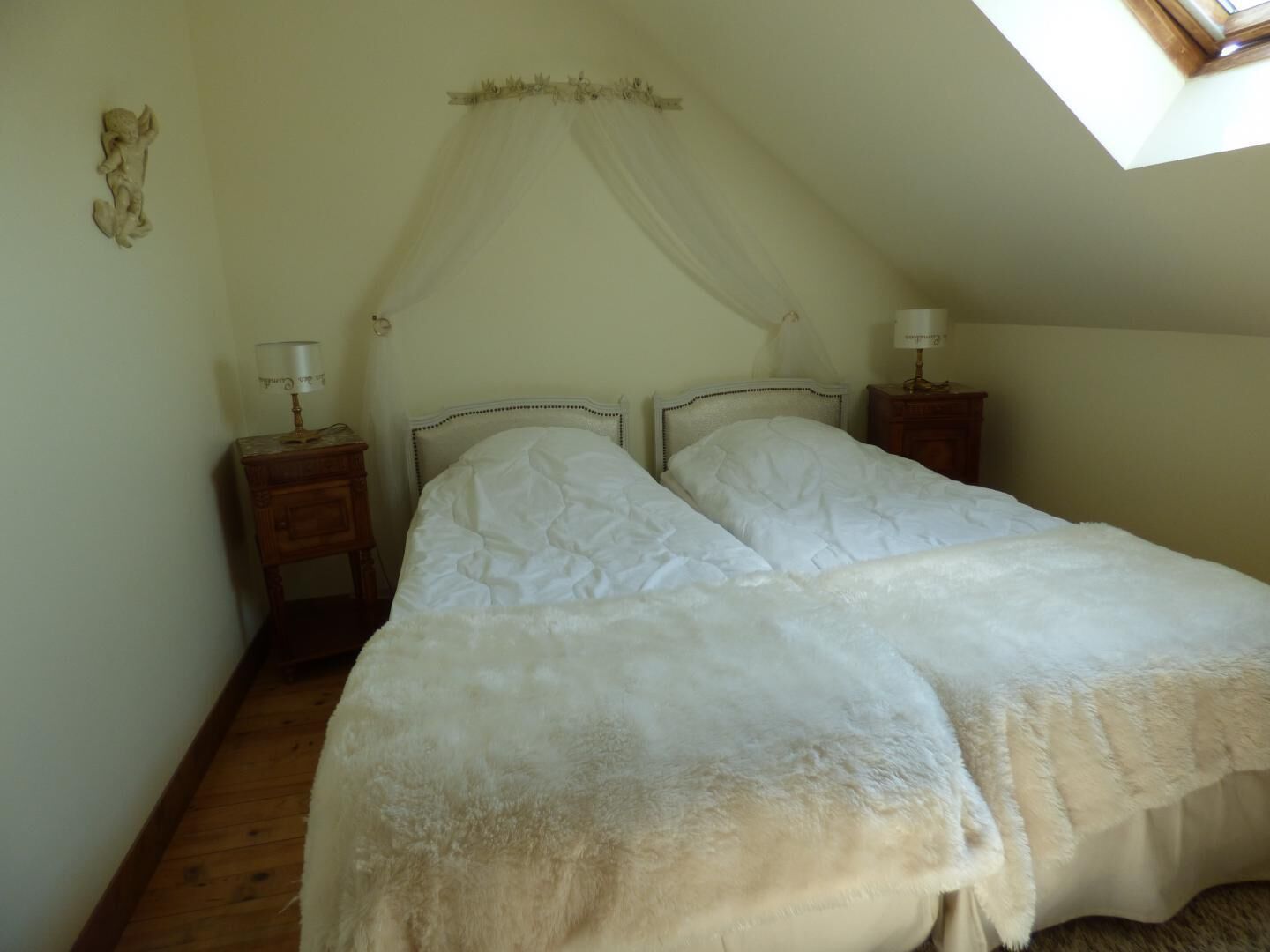 A bedroom with two beds, a canopy bed, wooden nightstands, and a skylight.