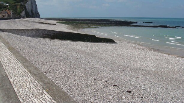 A pebble beach with a cliff, a paved walkway, and a view of the sea. - Gîtes de France® - Le Clos des Camélias (VEULETTES SUR MER)