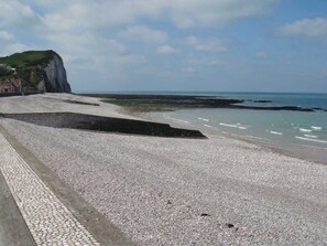 Une plage de galets bordée d’une falaise, avec une promenade dallée et une vue sur la mer.