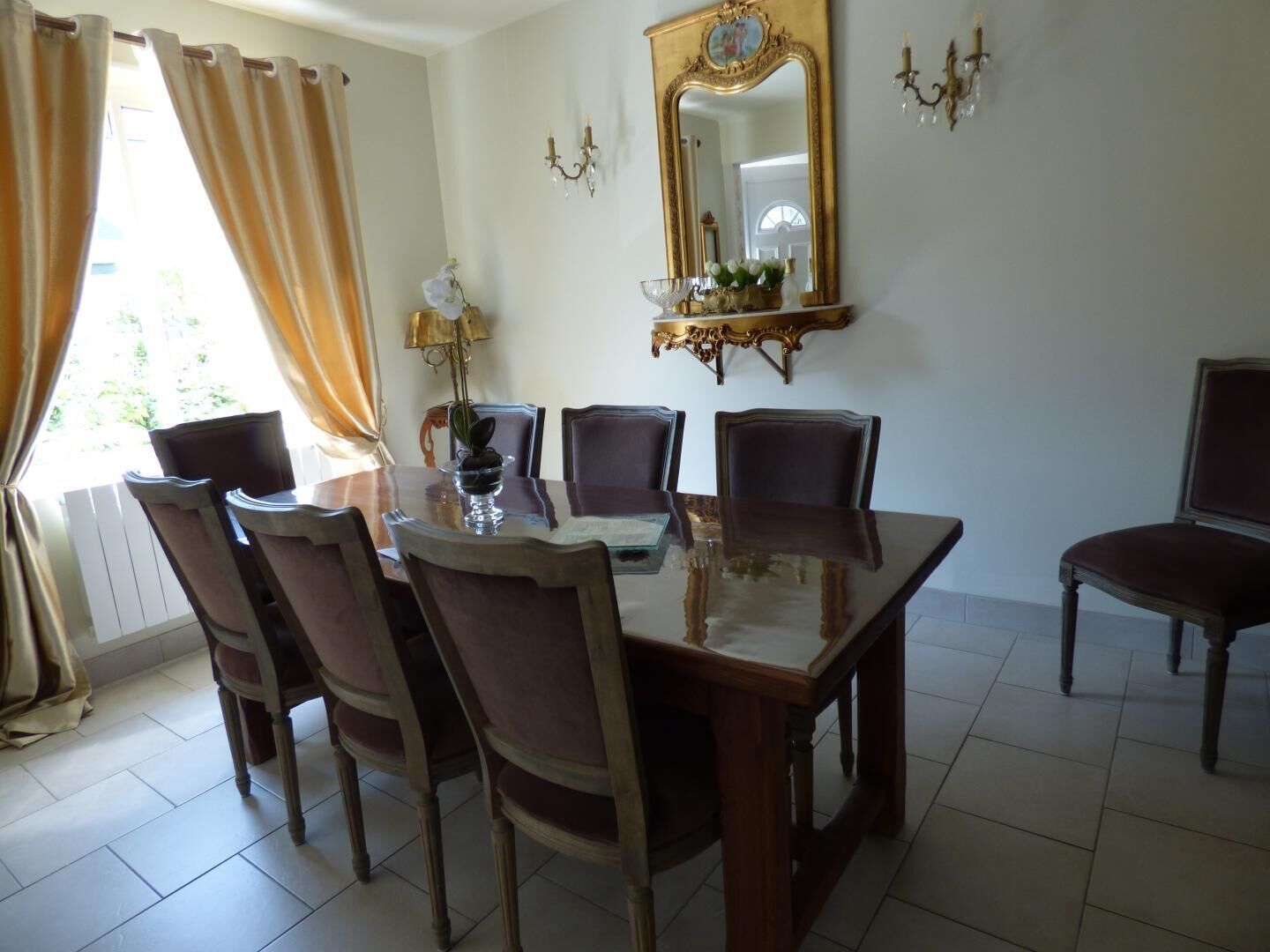 Una sala da pranzo con un tavolo rettangolare, sei sedie, un lampadario, uno specchio a parete e una finestra con tende.