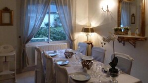 A dining area with a table set for four, a chandelier, and a large mirror on the wall. - Gîtes de France® - Le Clos des Camélias (VEULETTES SUR MER)