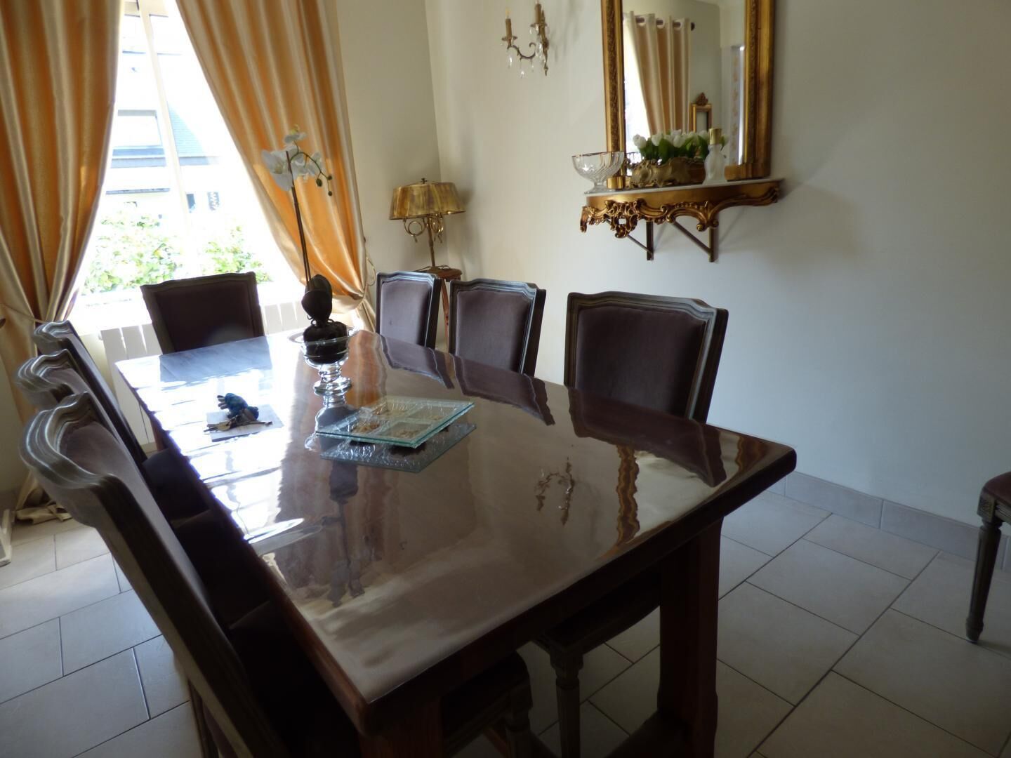 A dining area with a large table, chairs, a chandelier, and a mirror.