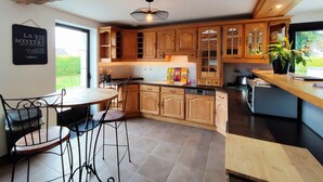 A modern kitchen with wooden cabinets, a dining area with metal chairs, and a large window providing natural light.
