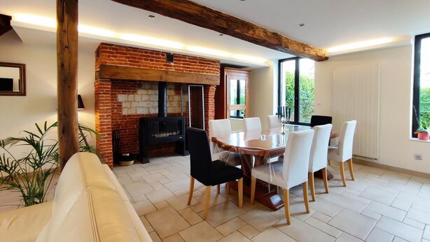 A dining area with a brick fireplace, white chairs, and a wooden table.
