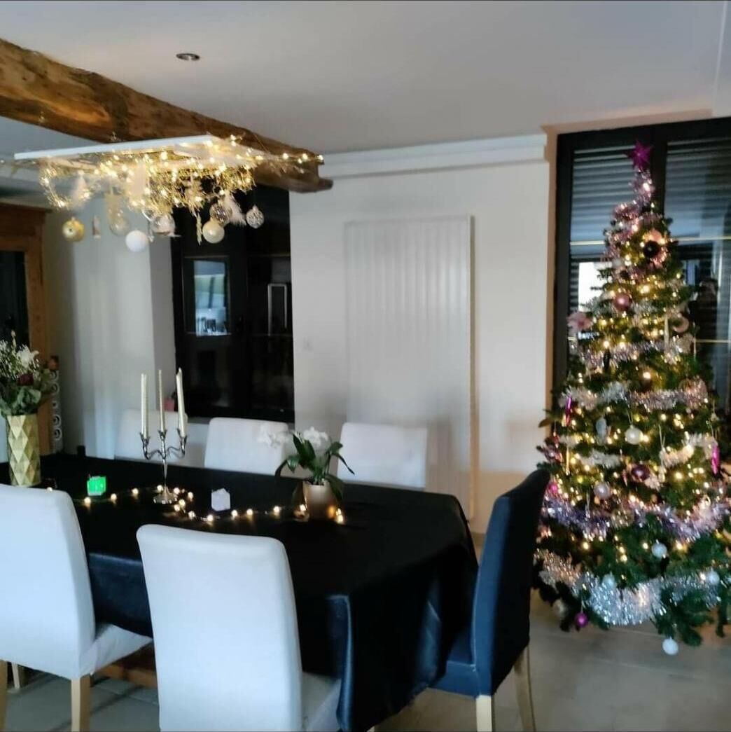 Comedor con mantel negro, sillas blancas y un árbol de Navidad con luces.