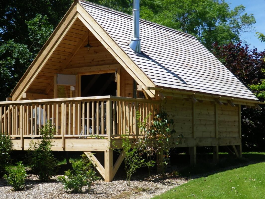 Une cabane en bois dotée d’un balcon, d’une cheminée et d’un petit espace porche.