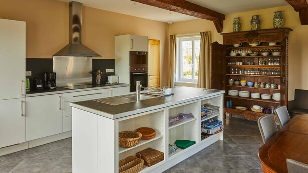 A modern kitchen with white cabinetry, a stainless steel range hood, and a built-in island with storage shelves.