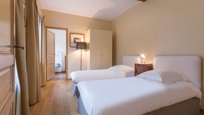 A hotel room with two beds, a wardrobe, a lamp, and a door leading to another room.