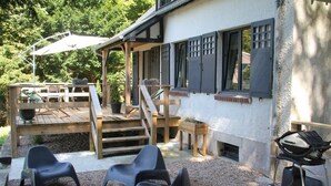 A covered outdoor seating area with a wooden deck, a barbecue grill, and black plastic chairs.