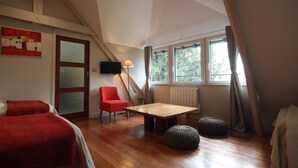 A cozy attic bedroom with a wooden floor, a red chair, a small table, and two ottomans.