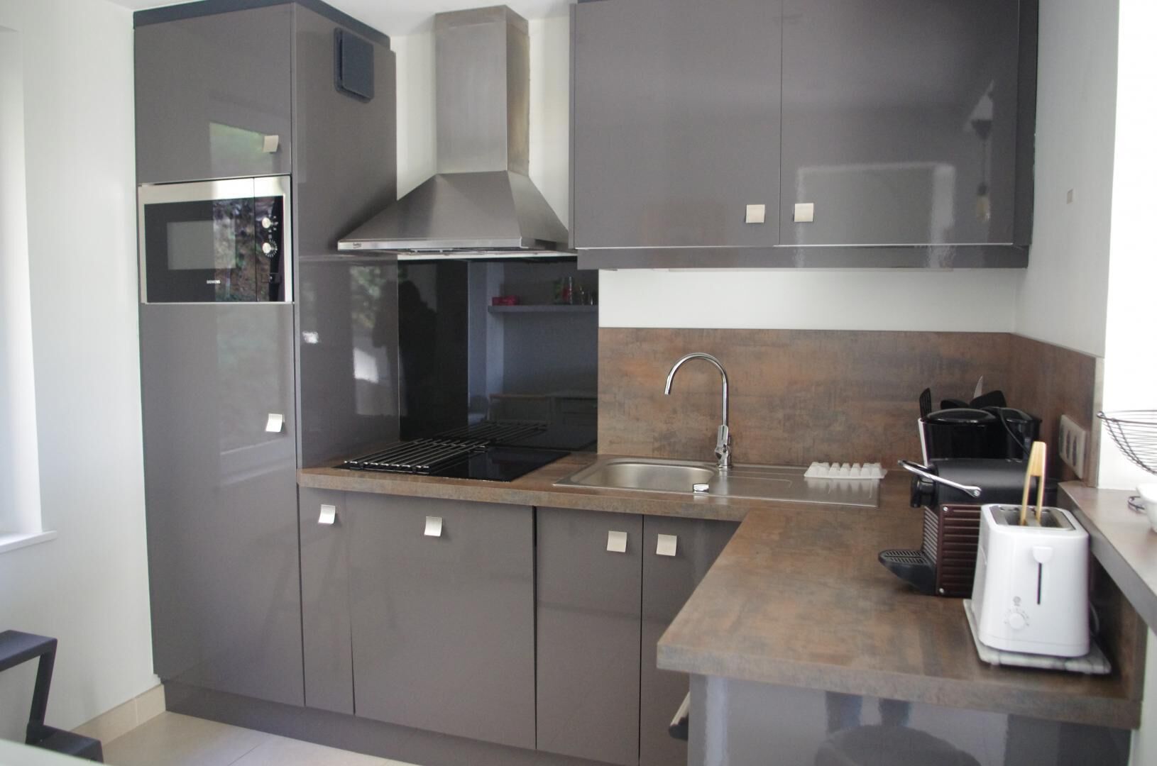 Una cucina moderna con forno integrato, pensili in acciaio inossidabile, cappa aspirante, lavello e tostapane.