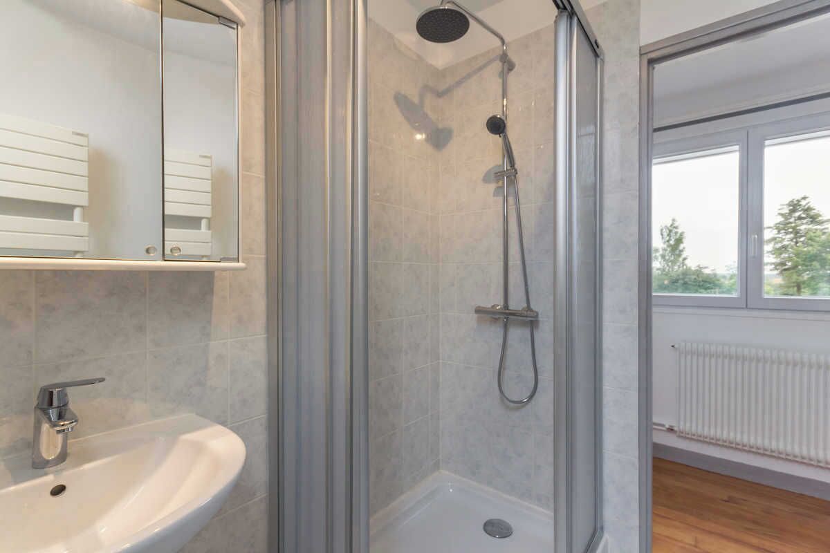 A modern bathroom with a glass-enclosed shower, a white sink, and a window providing natural light.