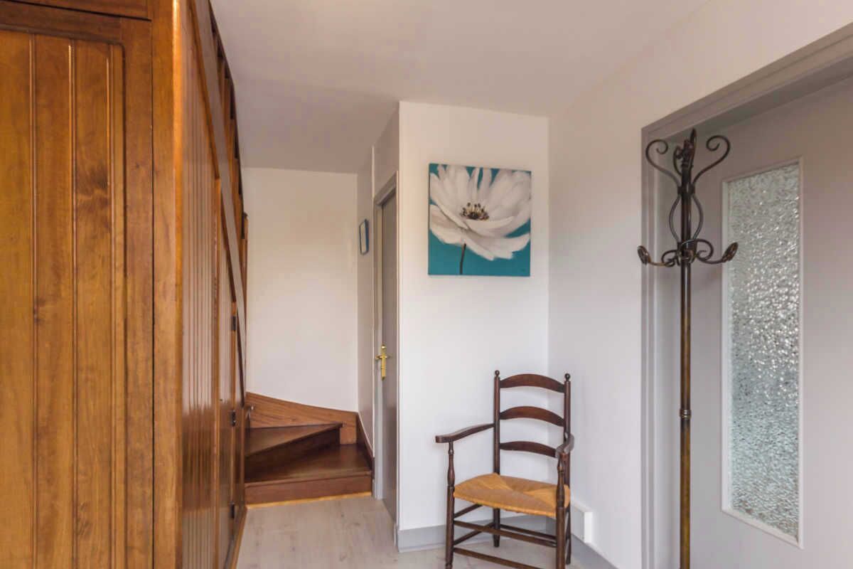 Un escalier en bois mène à une pièce dont un des murs est blanc et qui est décorée d’un tableau représentant des fleurs, encadré.